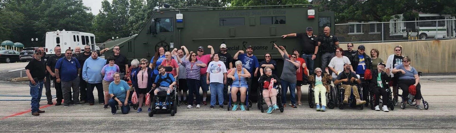 A group of people smiling and holding up their fists in front of a Special Response Team vehicle.
